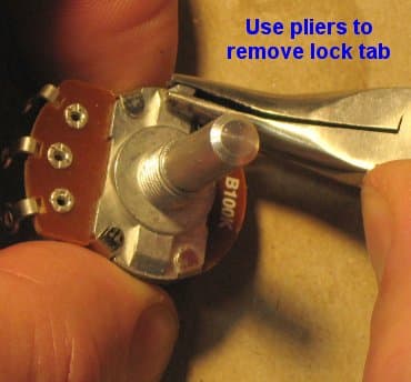 Pliers gripping the break-off tab low on a regular-sized pot, ready to twist it off.