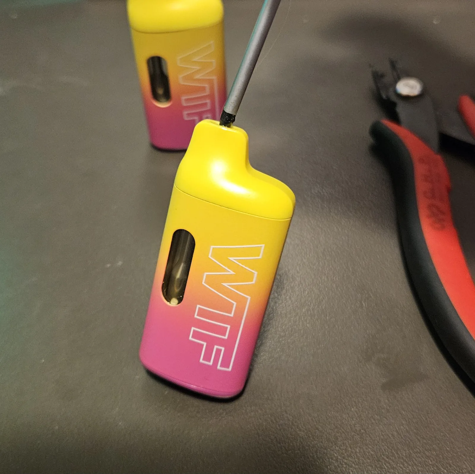 A WTF vape lying on the bench with a pry tool worked into the seam at its top, starting to split the plastic housing.
