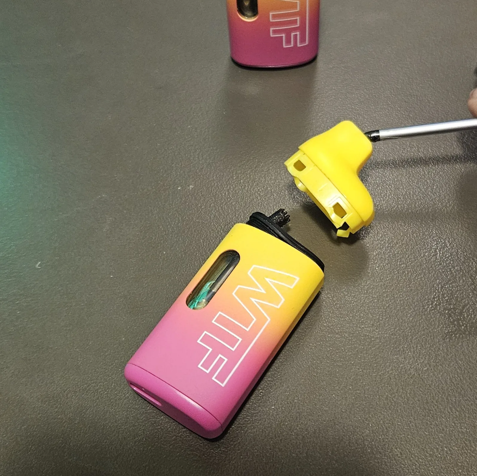 The vape with its top end cap pried off and separated from the body.