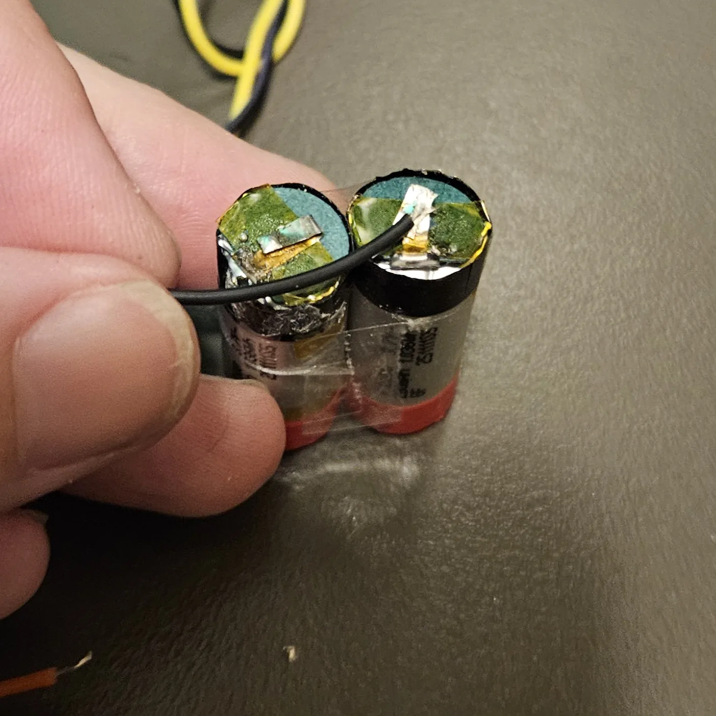 The two cells held side by side with a black wire bridging their two negative terminals.