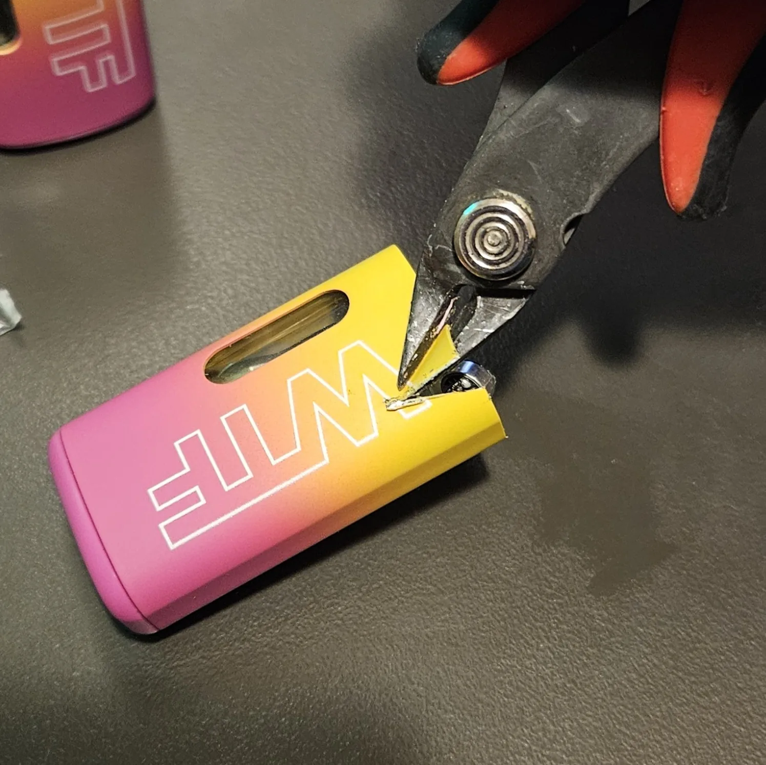 Cutters nipping the metal terminal tab at the top of the freed cell.
