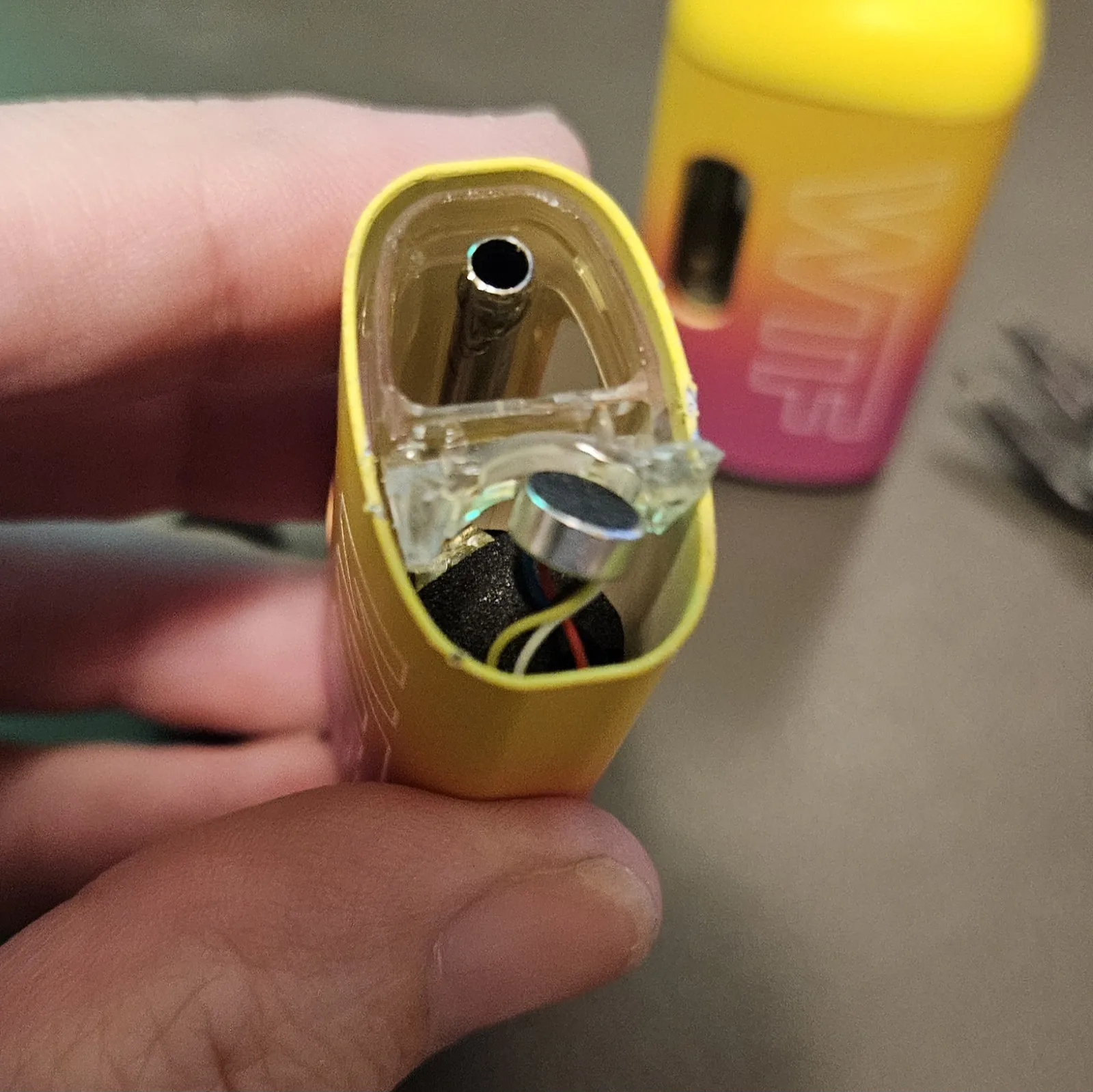 A hand holding the opened vape shell, the clear internals and the lithium cell now visible inside.