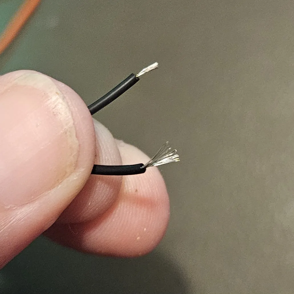 Fingertips holding two black wire ends, the stripped tips freshly tinned silver with solder.