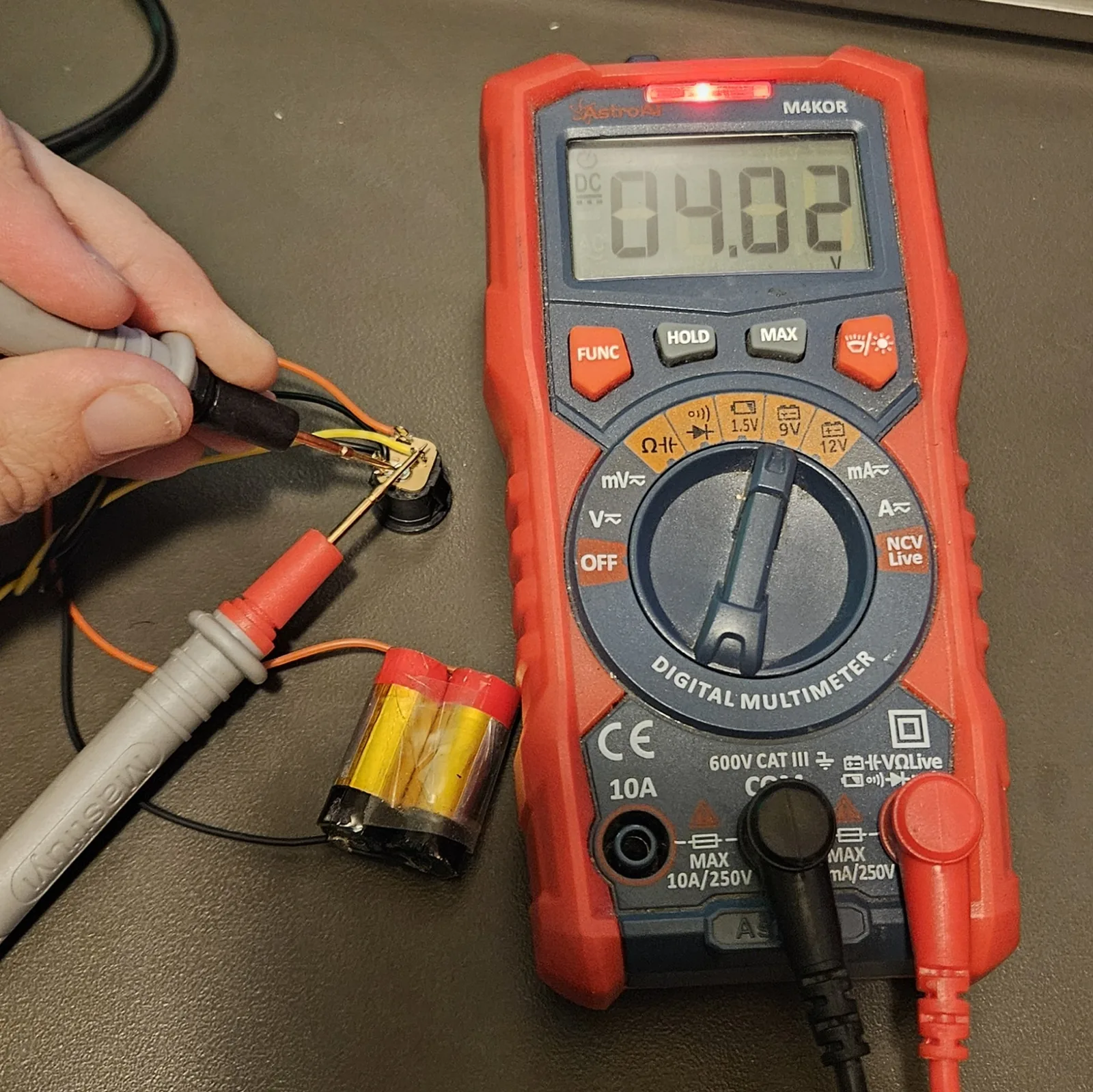 Testing the pack with a red digital multimeter — the screen reads 4.02 volts.