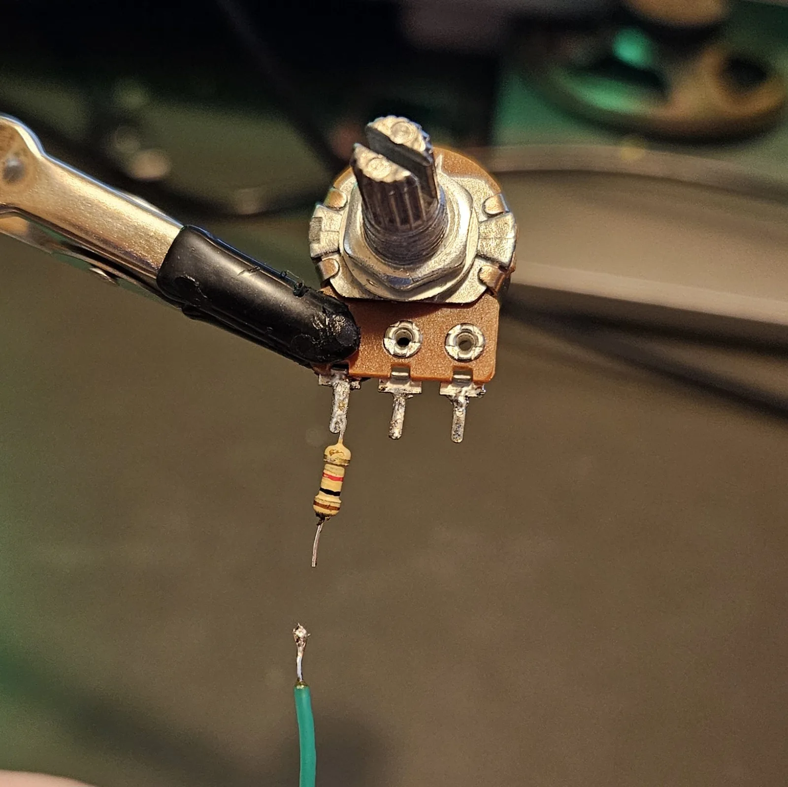 The same potentiometer with the resistor now soldered onto its outer lug and hanging straight down, while a green wire waits below with its tinned end pointing up.