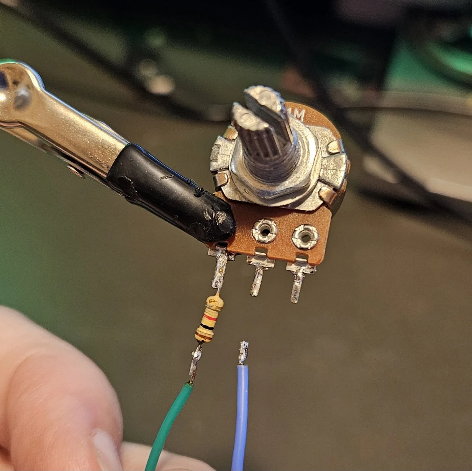 The potentiometer with its resistor attached and a green wire soldered to the end of that resistor, plus a second blue wire tinned and waiting alongside.