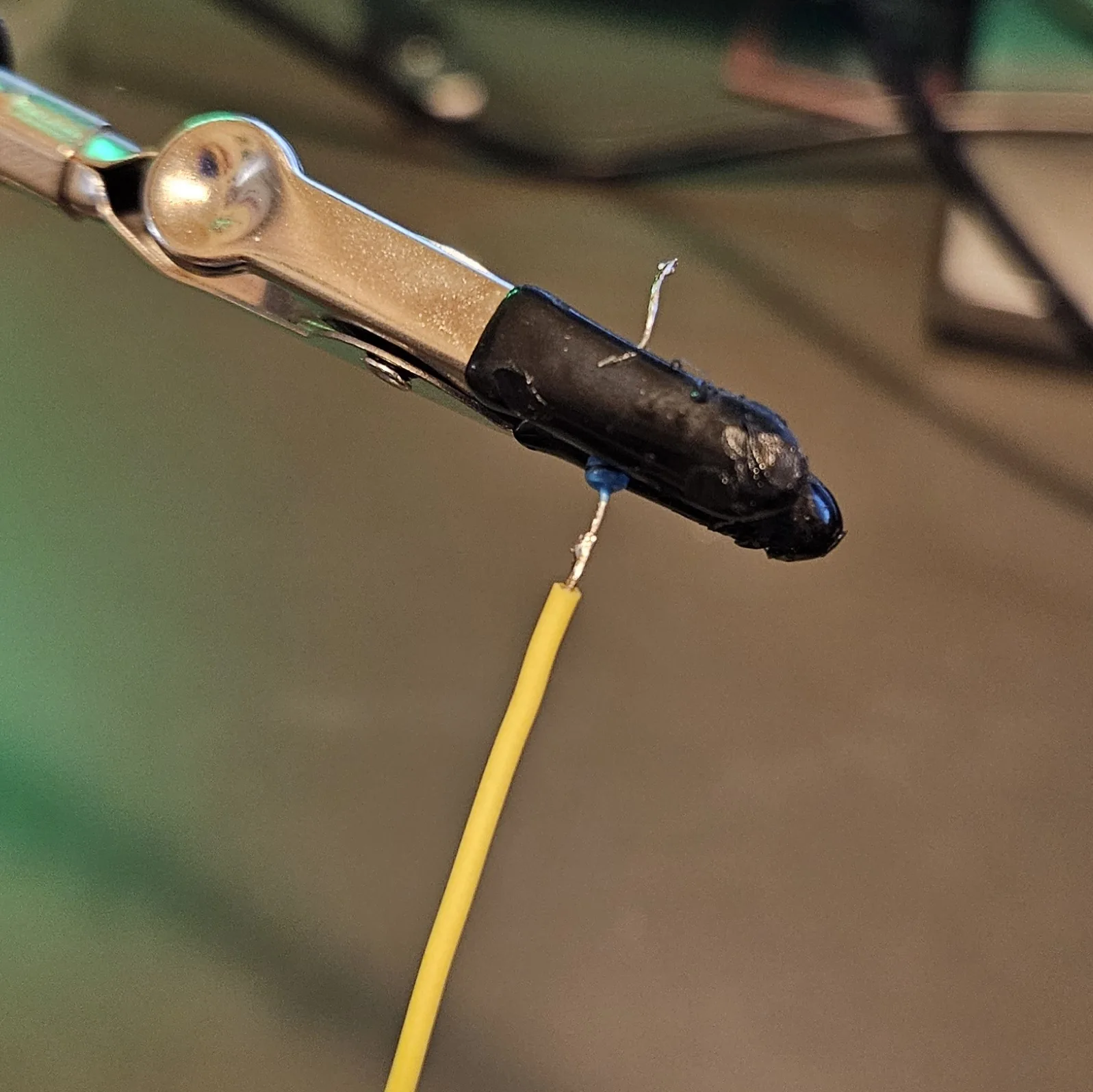 A close-up of a finished joint held in the clip: a yellow wire soldered onto a component lead, the connection covered in a neat bead of solder.