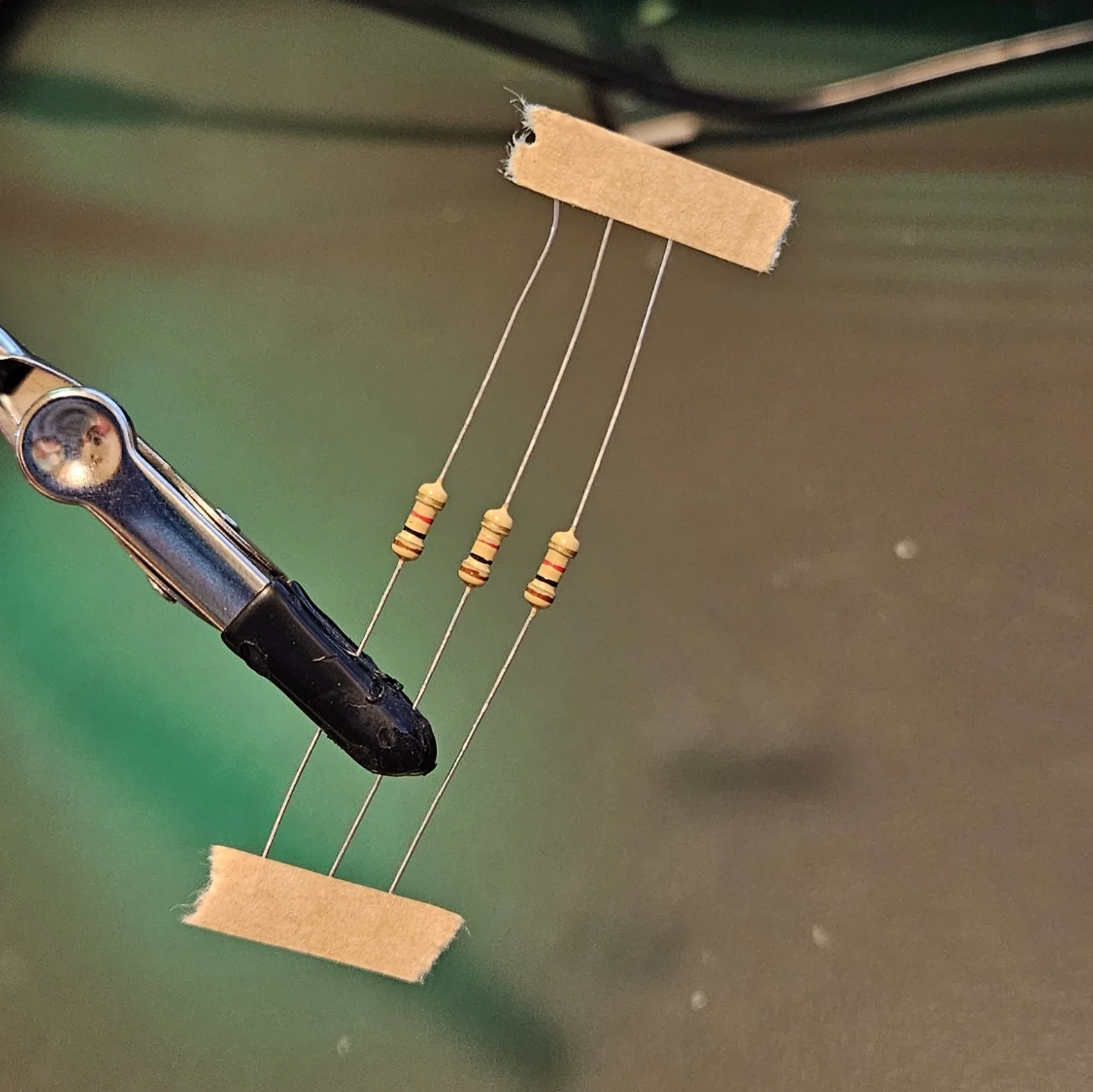 Three colour-banded resistors suspended between two strips of tape, their long leads running top to bottom.