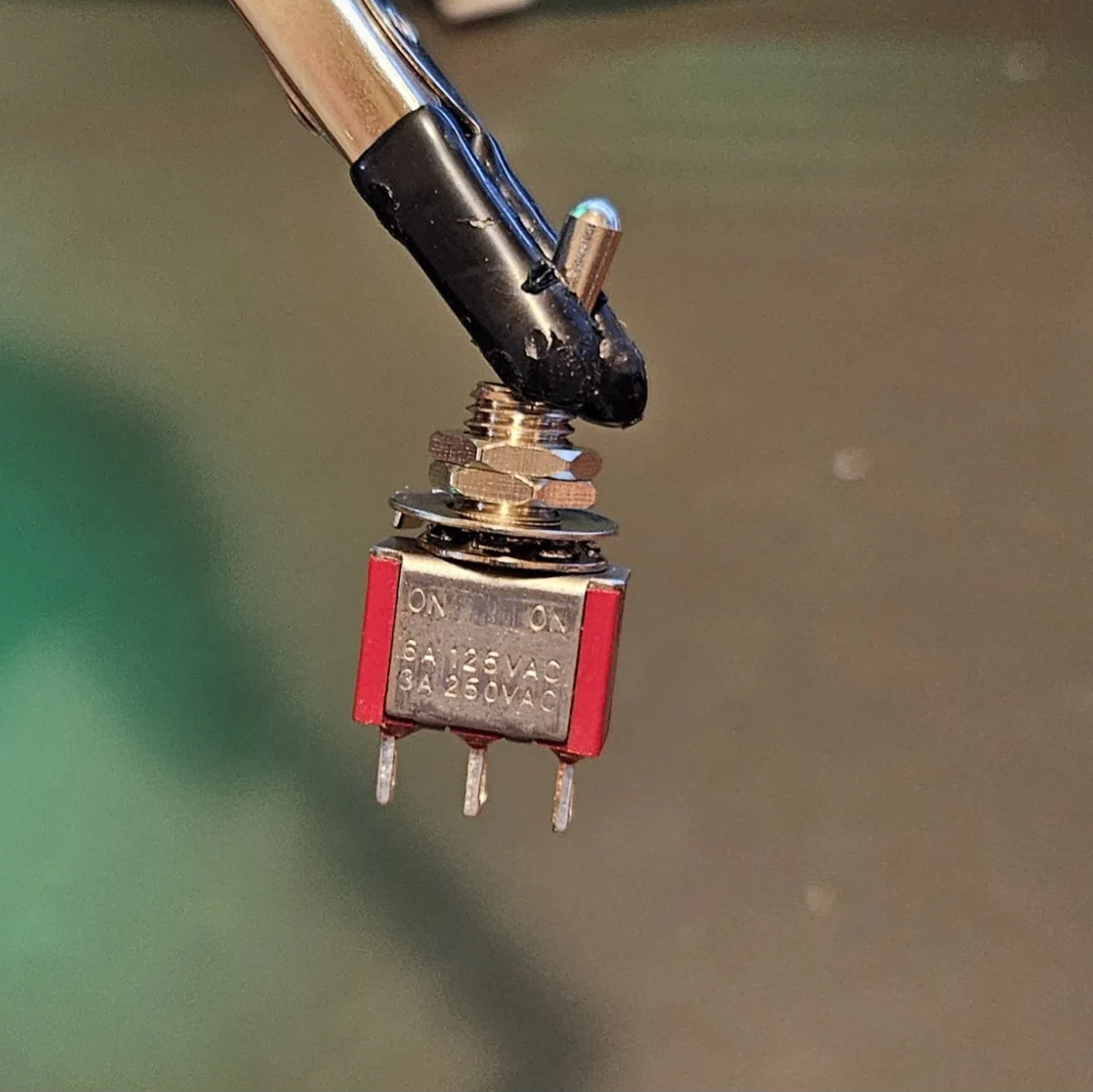 A small SPST toggle switch with its threaded bushing, nut and two solder lugs.