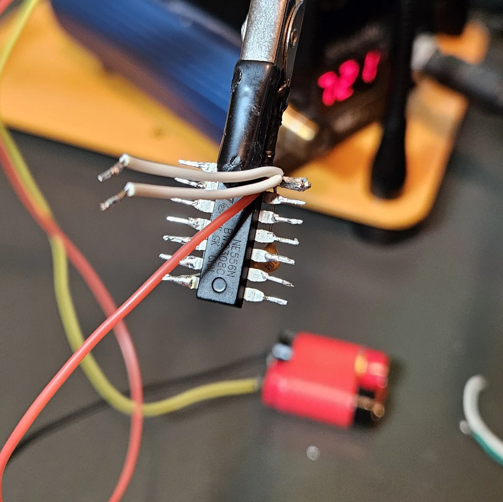 The white reset jumper wires and the red V-plus rail laid across the NE556's pins, positioned but not yet soldered.