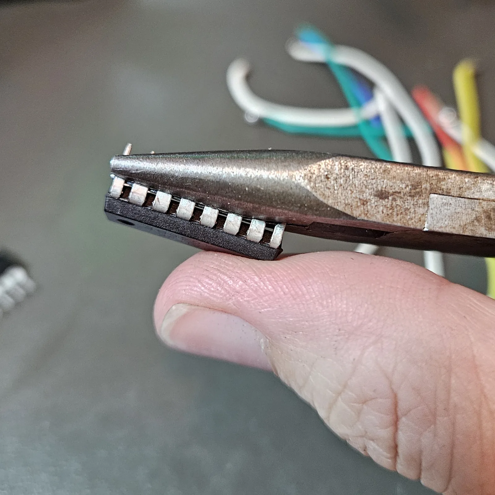 Needle-nose pliers bending the NE556's two rows of pins outward and flat against a thumb, splaying the legs so the chip will lie flat for dead-bug wiring.