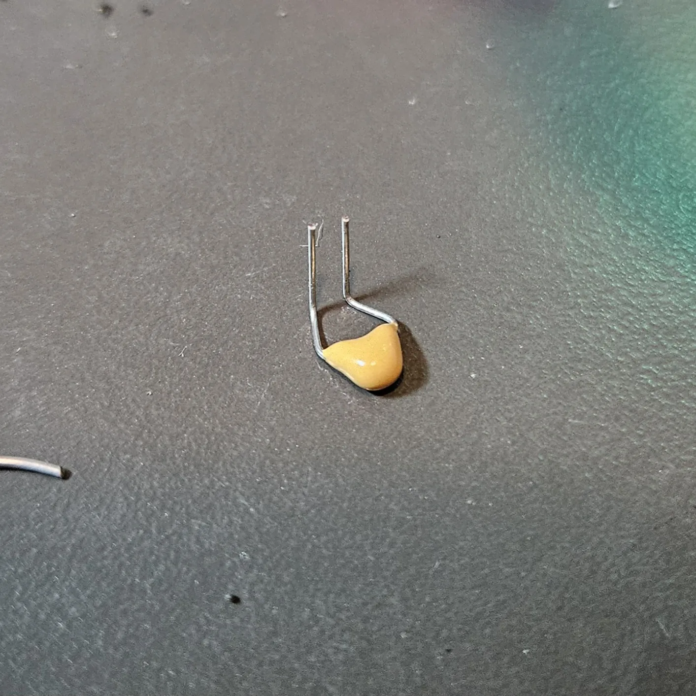 A single yellow 0.01 microfarad ceramic timing capacitor on the mat, its leads pre-bent into a U so it can bridge two pins down to ground.