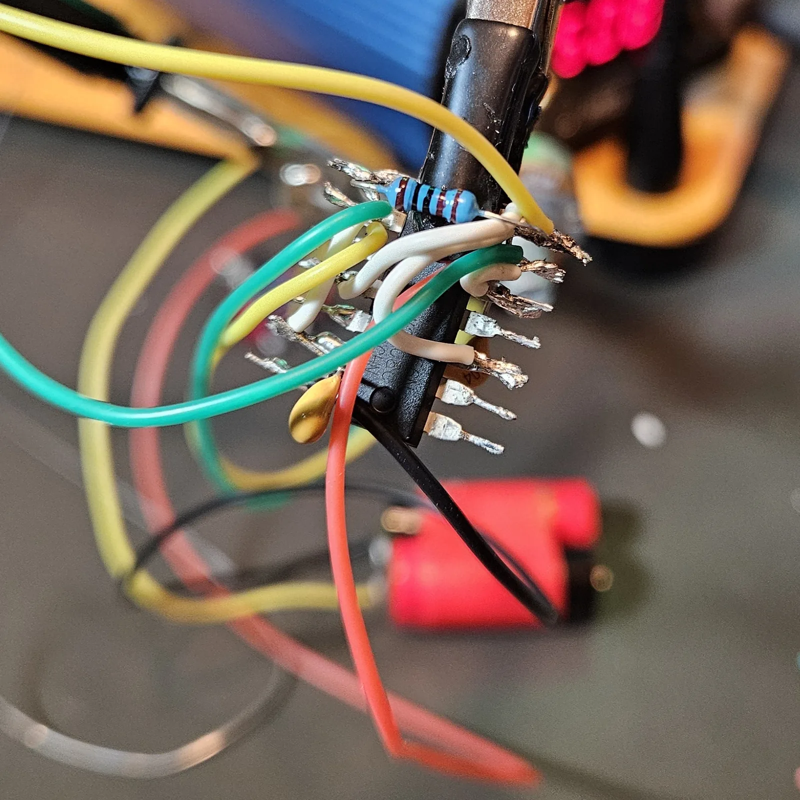 Dense point-to-point wiring building up on the chip: green and yellow pot leads, white jumpers, the red V-plus rail, the blue 1K resistor, and a yellow timing cap all converging on the pins.