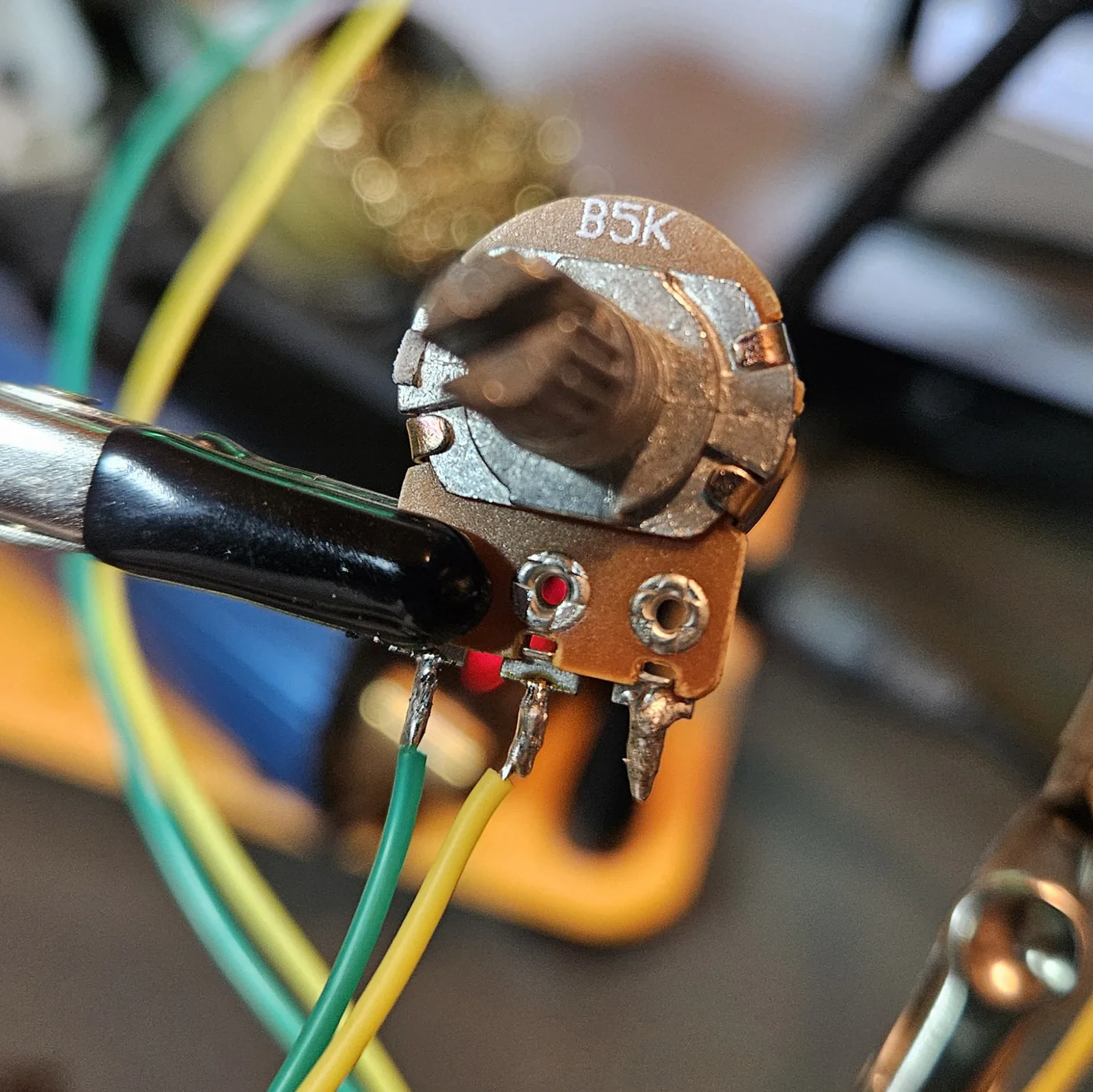 The B5K volume potentiometer clamped in the helping hands with green and yellow leads soldered to two of its lugs, back label reading B5K.