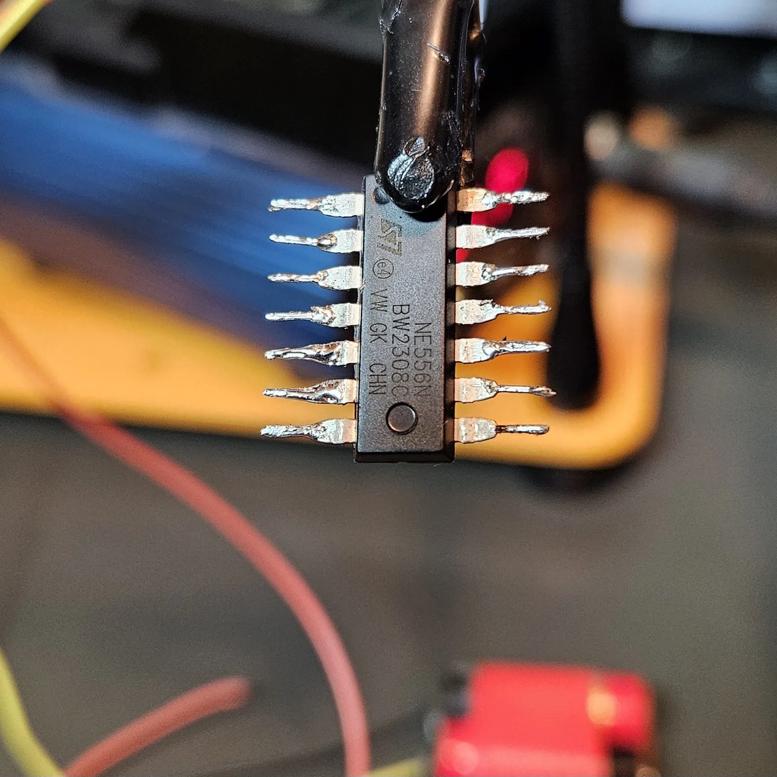 A soldering iron tinning the row of splayed NE556 pins one at a time, each leg taking a small bright bead of solder.