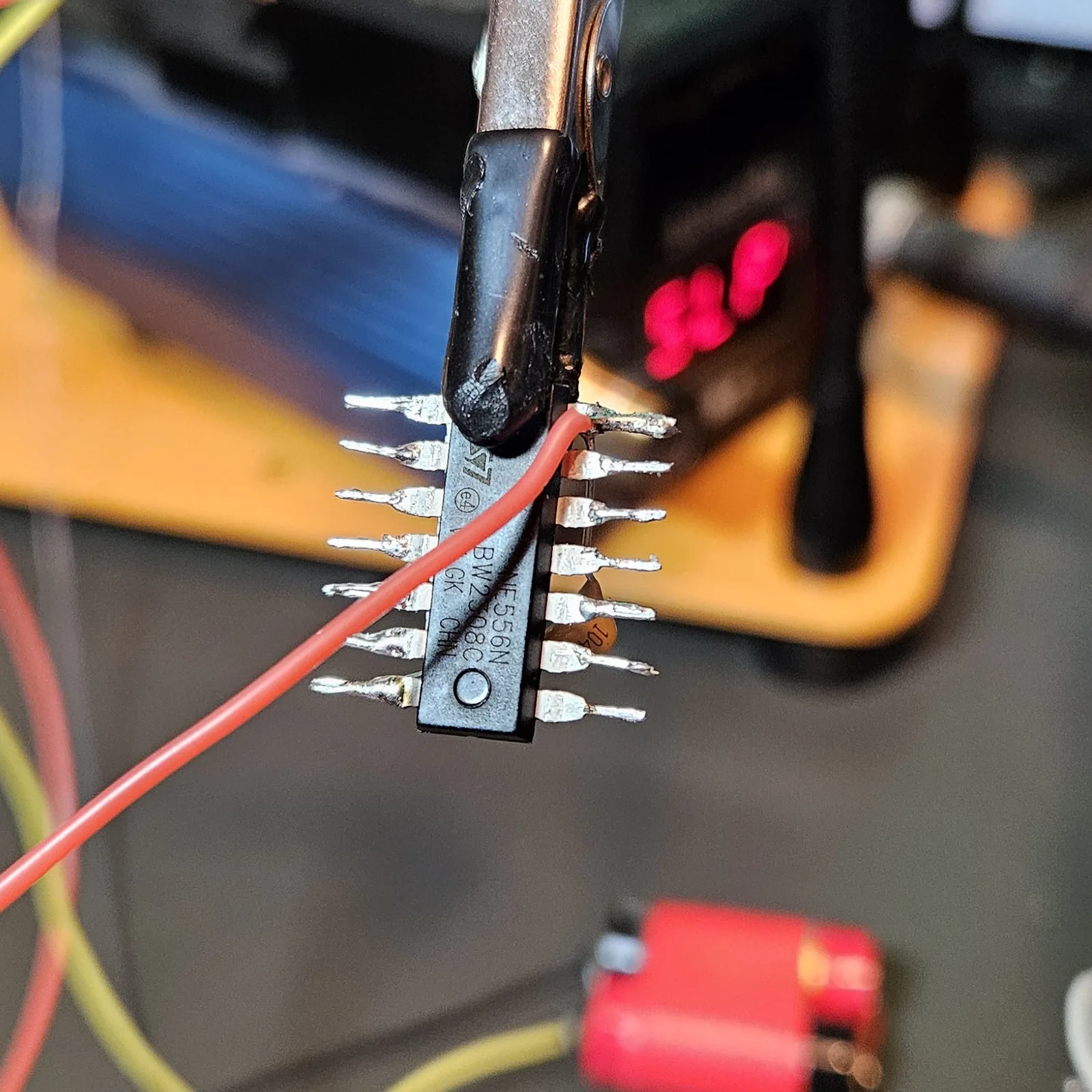 A red V-plus wire soldered across the chip distributing the positive supply along the pins, with the '104' decoupling cap visible.