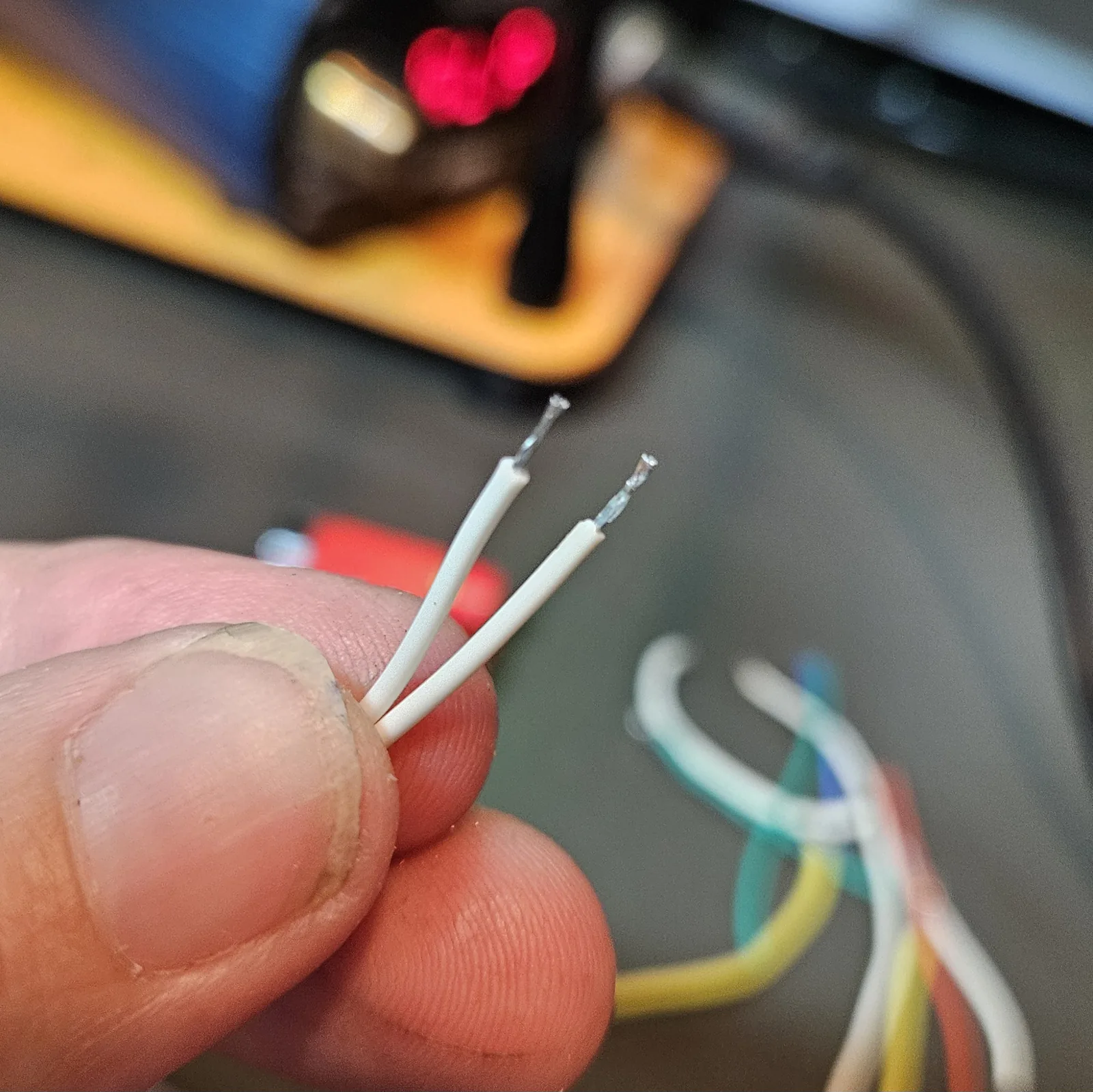 Two short white jumper wires, stripped and freshly tinned at both ends, held in fingers ready for the reset connections.