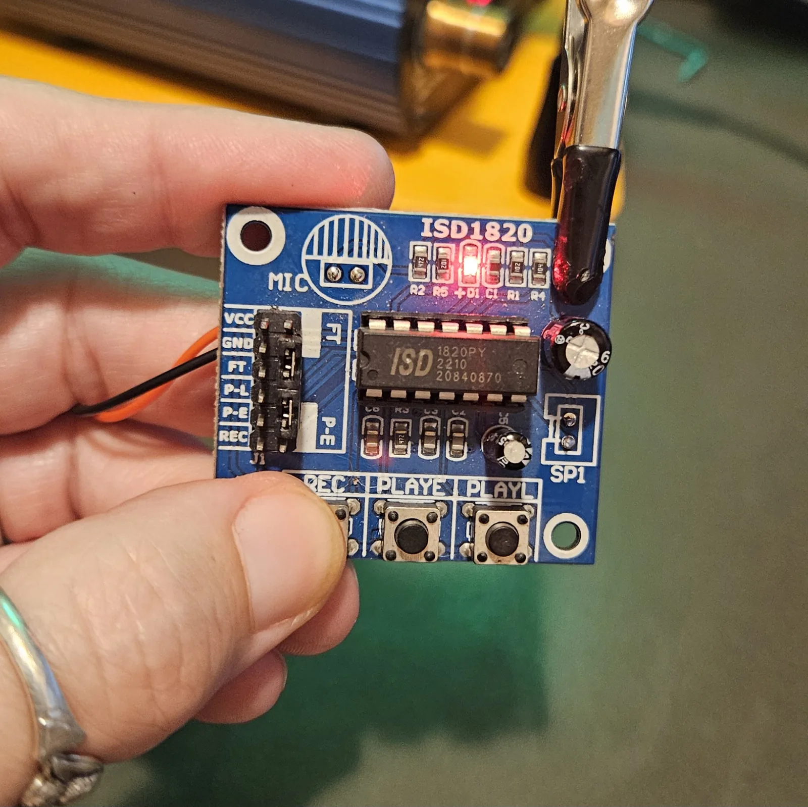 The front of the powered module held between finger and thumb. The small red D1 indicator LED on the top edge is lit, showing the board has power.