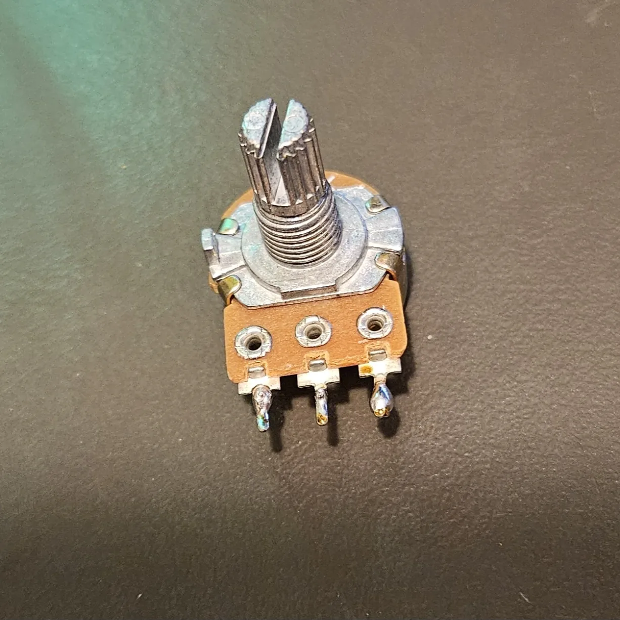 A bare potentiometer standing on the bench, seen from the front, with its splined shaft, threaded bushing and three solder lugs along the bottom edge.