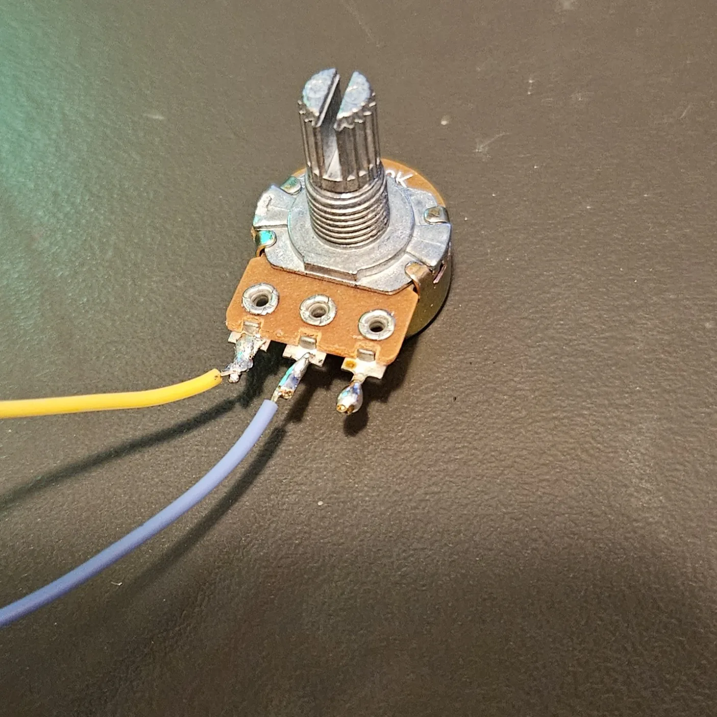 Close-up of the potentiometer with two wires soldered on, a yellow lead on one outer lug and a grey lead on the centre wiper lug, the third lug left bare.