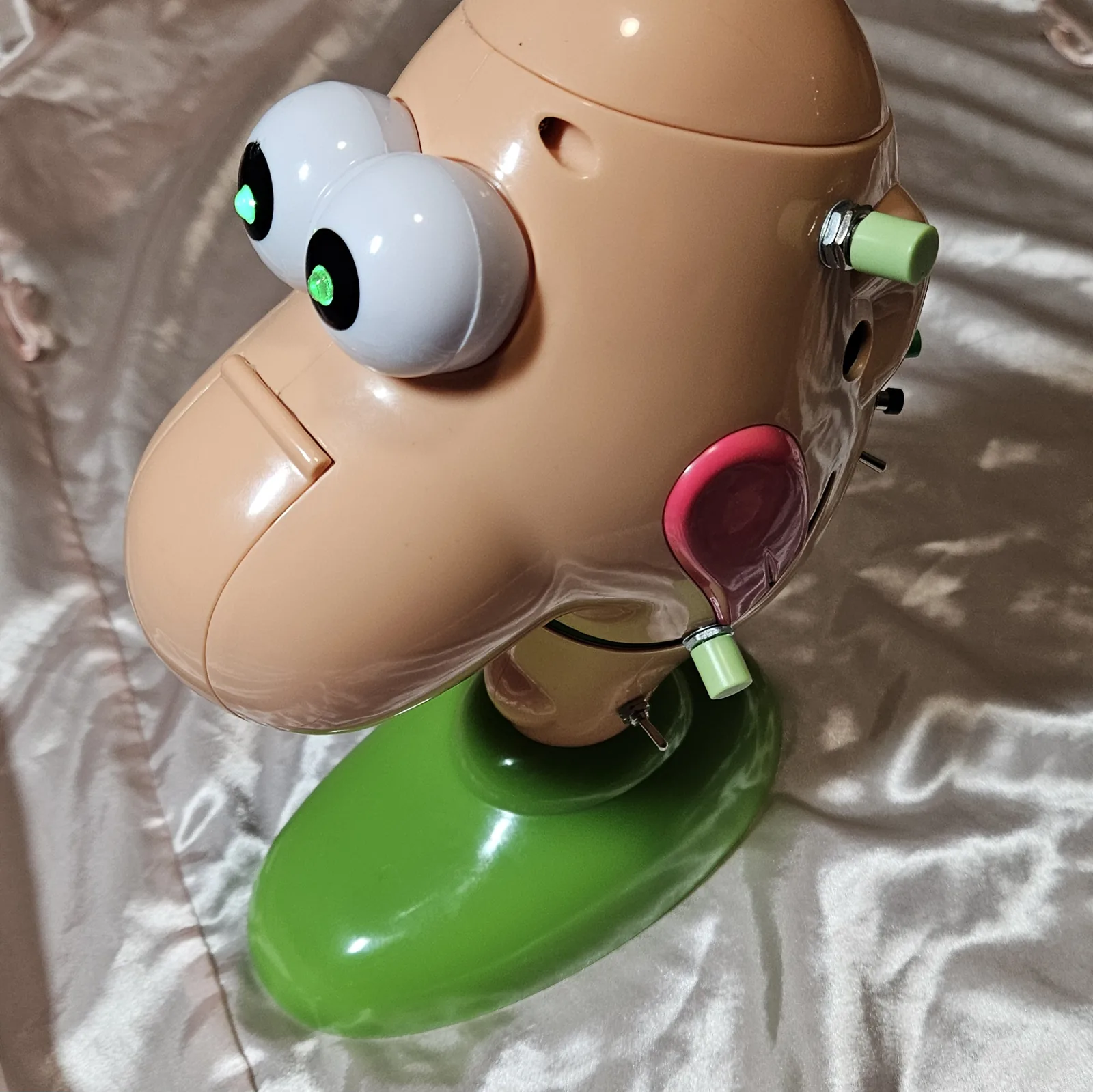 The finished box from above and behind, eyes lit green: the added hardware runs down the right side of the head - the green pitch knob high on the back of the skull, then the green record button, the black play button and the loop toggle below it. The green volume knob is mounted low near the tongue, with the power switch just above the green base.