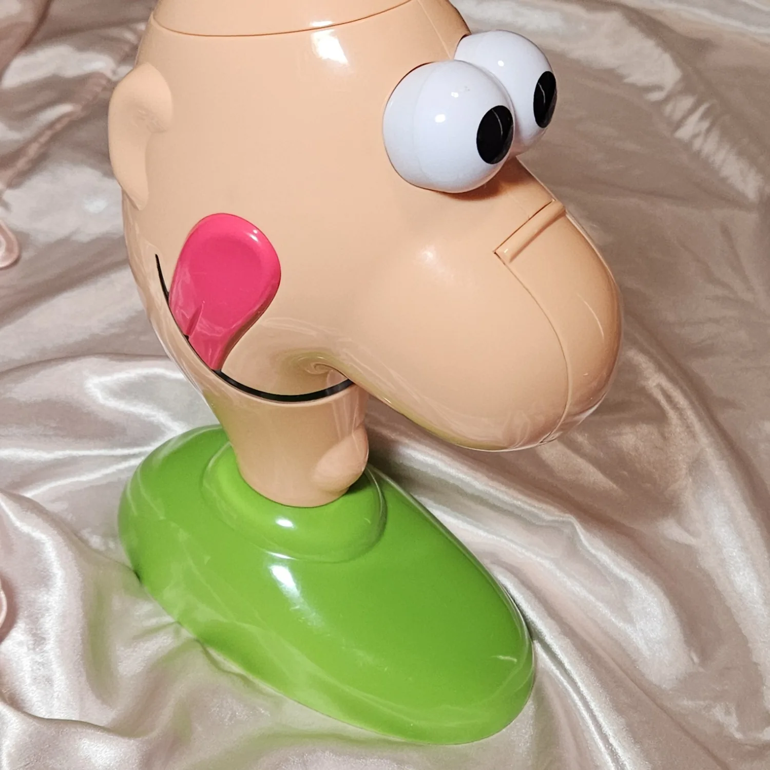 The donor toy before any work: the same flesh-toned Gooey Louie head on its green oval base, completely unmodified. The googly eyes are plain white with black pupils and no lights, the pink tongue hangs from the mouth, and the smooth plastic has no holes, knobs or switches anywhere.