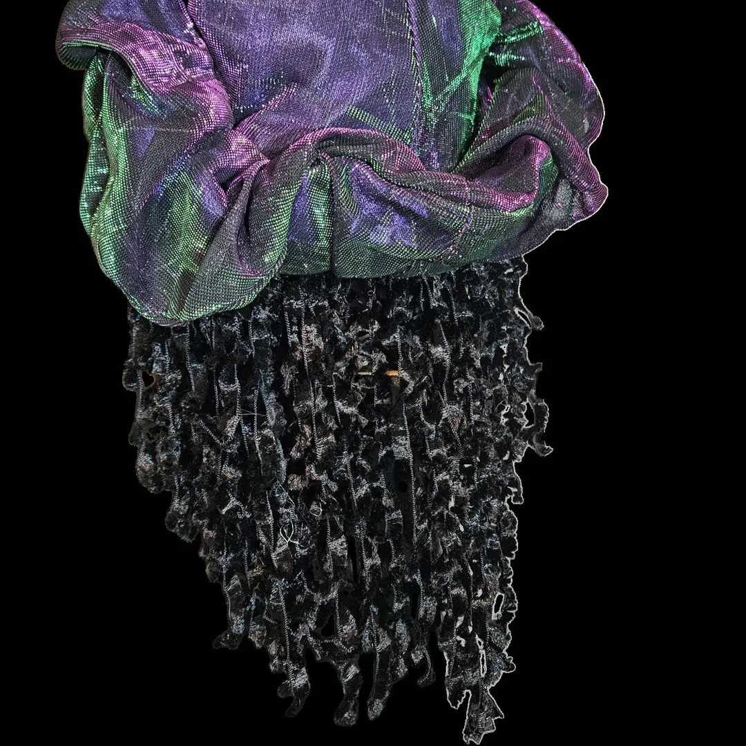 Back of the head against black — no face visible. The iridescent purple-and-green cap gathers over the crown, and the black crushed-velvet ringlets hang below it in long ragged strands.