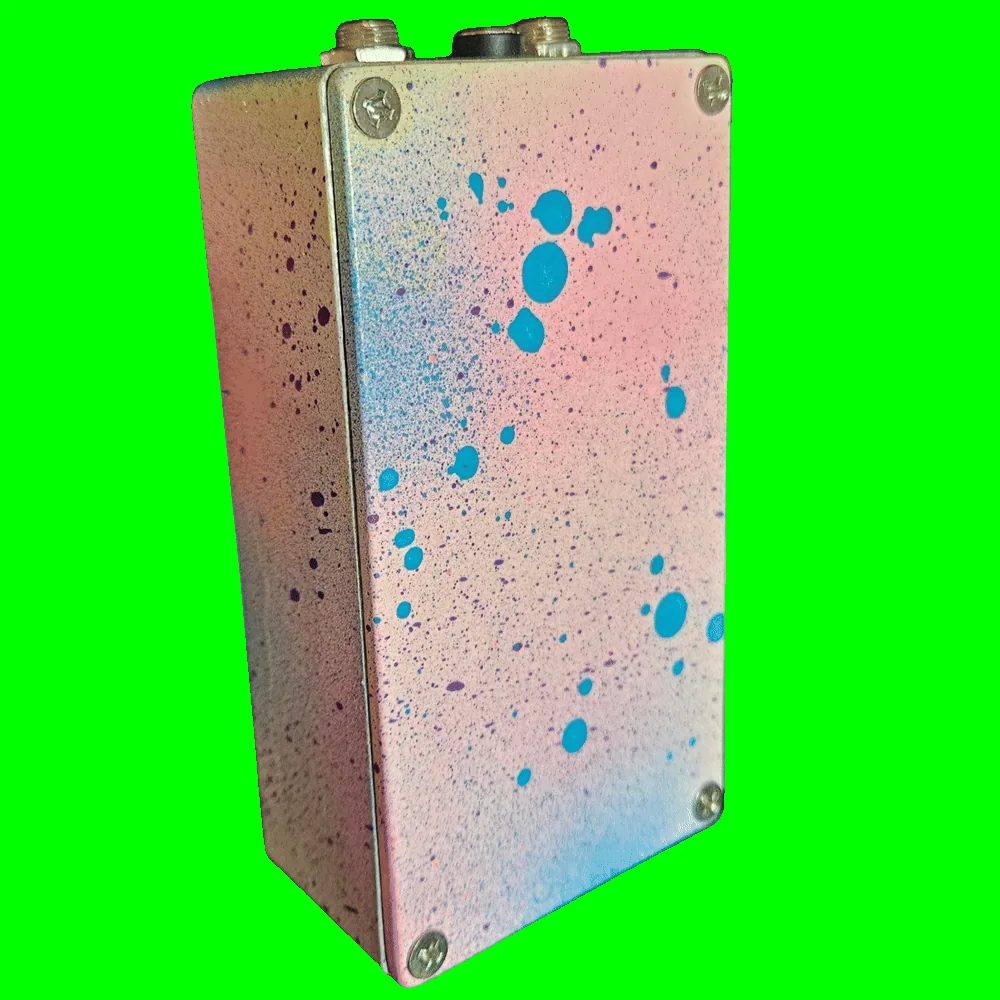 Back of the pedal: the bottom plate carries the same pink-and-blue speckle with bold turquoise droplets and a Phillips screw in each corner, with no label or serial plate. The two jacks and the DC socket are visible along the top edge.