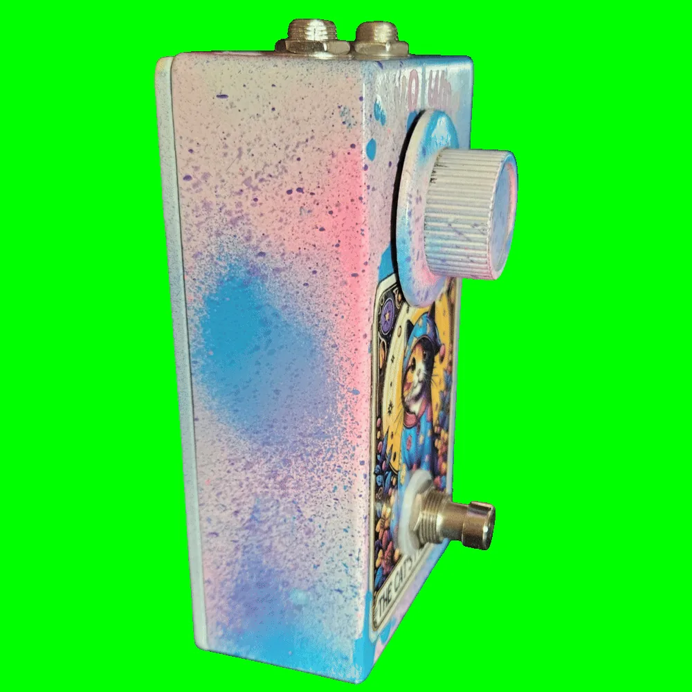 Left side of the pedal: a plain wall of pink, blue, and purple speckle over white with no jacks or controls on this face. The light-blue knob and the footswitch stand well proud of the front, and the two top-edge jacks show along the upper corner.
