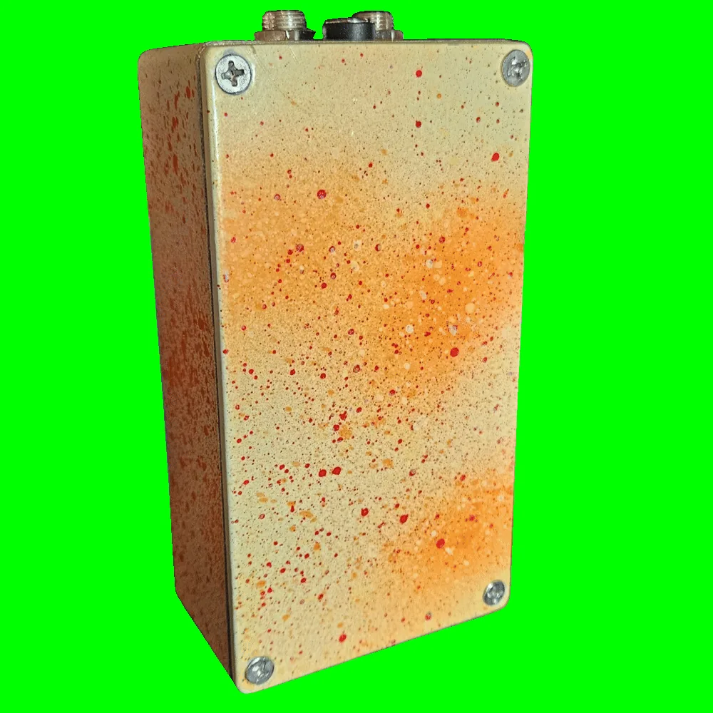 Back of the pedal: the bottom plate is cream misted with orange and spattered with fine red dots, with a Phillips screw in each corner and no label. The jacks and DC socket show along the top edge.