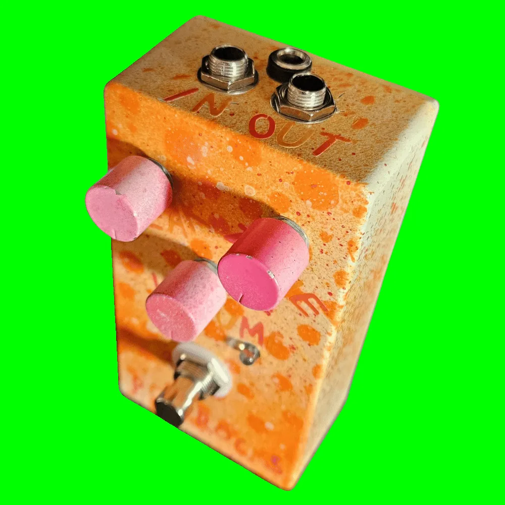 Top-down view of the enclosure: hand-lettered orange "IN" marks the left 1/4-inch jack and "OUT" the right, with a DC power jack set between and slightly behind them. The three pink knobs and the footswitch fall away below.