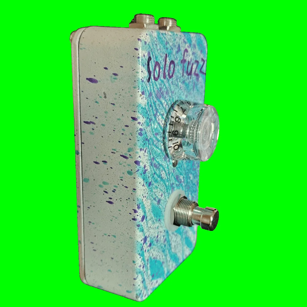 Left side of the pedal: a cream wall flecked with purple and teal, showing the clear knob &mdash; its skirt numbered around the edge up to 10 &mdash; standing off the face, with the footswitch below it on a white washer.